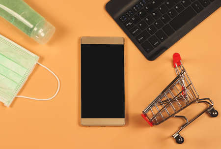 Top view of mobile phone , shopping cart,computer keyboard , medical mask and sanitizer gel on orange background . Covid19 prevention , new normal and online shopping.の写真素材