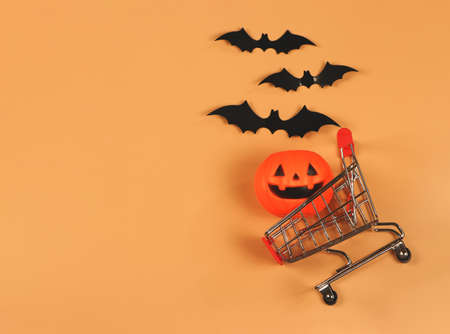 Top view or flat lay of  Halloween pumpkin on shopping cart  with black paper bats on orange background with copy space. Halloween holiday concept.の写真素材