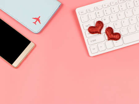 Top view or flat lay of red glitter heart on compuer keyboard , mobile phone and passport cover on pink background with copy space ,long distance love and online dating concept.の写真素材