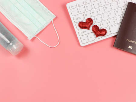 Top view or flat lay of red  heart on computer keyboard , passport, medical  face mask and sanitizer gel on pink background. Covid19 prevention, new normal and long distance love.の写真素材