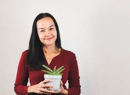 Portrait of pretty Asian woman in red long sleeve  t-shirt holding  a plant pot with sansevieria,...