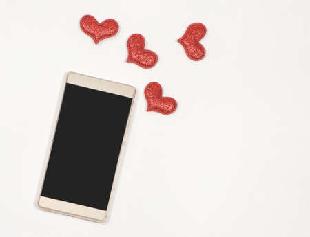 Top view or flat lay of blank screen mobile phone on white background decorated with red glitter hearts and copy space. valentine's day,  communication , online dating concept.の写真素材