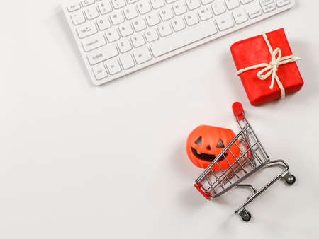 Top view or flat lay of  Halloween pumpkin on shopping cart, red gift box and computer keyboard  on white background with copy space. Halloween holiday and shopping online concept.の写真素材