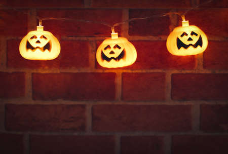 Dark image of Halloween pumpkin lights glowing , hanging on brick wall. Halloween decoration concept.の写真素材