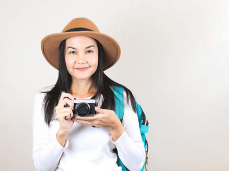 Portrait of Asian woman wearing  white t-shirt and hat , holding camera and carrying backpack, smiling and looking at camera. Travelling concept.の写真素材