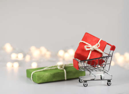 Front view of  red gift box  in shopping cart  on white background with green gift box  and  Christmas lights. Christmas  holiday shopping concept.の写真素材