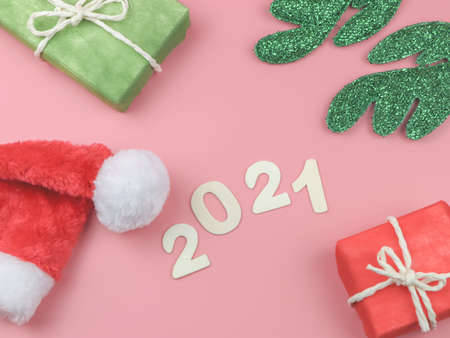 Top view or flat lay of wooden number 2021 on pink background with Christmas hat, green reindeer horn and gift boxes. Happy new year 2021 celebration.の写真素材