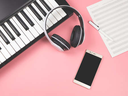 Top view or flat lay of  mobile phone , blank music sheet and  headphones on electric piano on pink background with copy space.Remote piano lessons concept.の写真素材