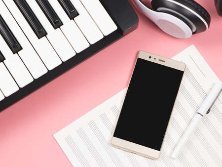 Top view or flat lay of mobile phone , blank music sheet , headphones and  electric piano on pink...