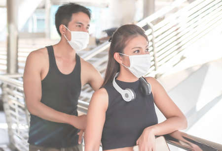 Asian woman and man in black sportswear wearing protective masks, standing in public walkway, looking away. selective focus on woman. .Covid-19 prevention, new normal and sports.の写真素材