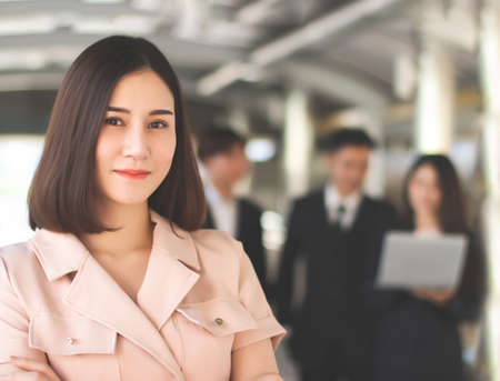 Close up image of confident beautiful Asian business woman in beige color  suit standing in front of her team, smiling and looking at camera.の写真素材