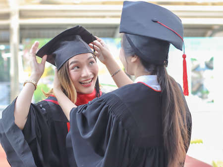 Two cheerful  graduated women in graduation gowns, helping each other dress up, smiling happily. ....