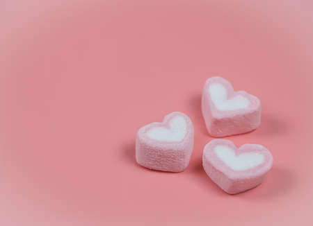 Close up image of Three heart shape marshmallows on pink background.
