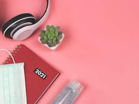 Top view of red diary or planner 2021 with medical face mask, alcohol sanitizer hand gel, headphones and succulent plant pot on pink background. New year 2021 planning, COVID19 prevention and new normal concept.の写真素材