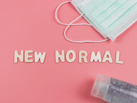 Top view or flat lay of wooden letters NEW NORMAL on pink background with medical face masks and alcohol sanitizer hand gel .  COVID-19 prevention and new normal concept.の写真素材