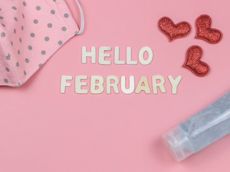 Top view or flat lay of wooden letters HELLO FEBRUARY  with  fabric mask, red glitter heart and alcohol sanitizer gel.   new normal and Valentine's day.の写真素材