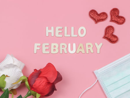 Top view or flat lay of wooden letters HELLO FEBRUARY  with medical face  mask, red glitter heart, white and red roses on pink background.   new normal and Valentine's day.の写真素材