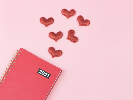 Top view or flat lay of red 2021 diary or planner and red glitter hearts decorated  on pink background with copy space. Love Valentine's day and new years.の写真素材