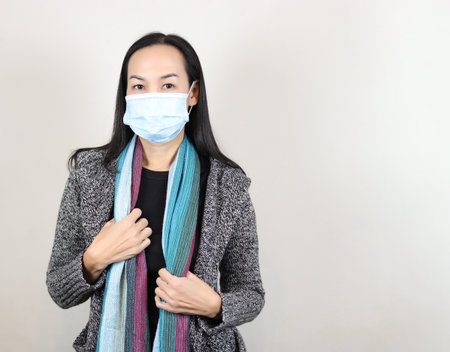 Portrait of Asain woman wearing medical face mask, winter coat and scarf standing on white background with copy space. Covid-19 prevention, new normal, winter portrait.の写真素材