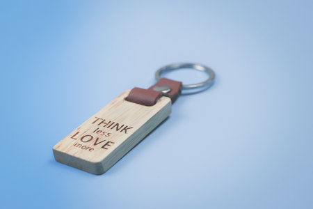 Close up of key chain with words "Think less love more" on blue background with copy space.の写真素材