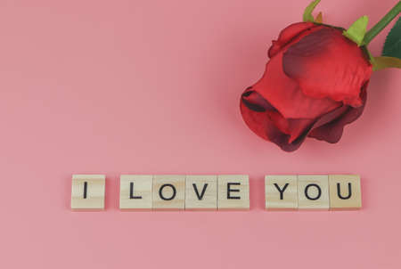 Top view or flat lay of wooden letters I LOVE YOU on pink background with red  rose. Valentine's day...