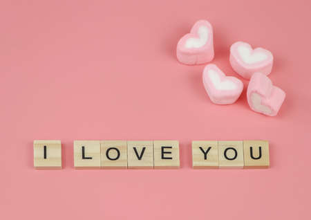 Top view or flat lay of wooden letters I LOVE YOU on pink background with heart shape marshmallows....