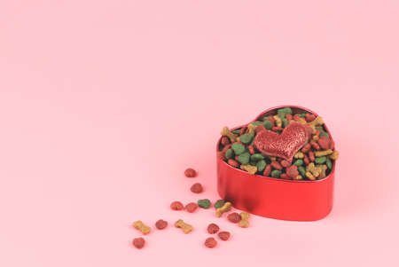 Front view  of dried dog food in red heart shape bow with red glitter heart on pink background. Valentine's day and pet lover concept.の写真素材