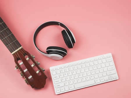 Top view or flat lay of computer keyboard, headphones and acoustic guitar on pink background with copy space. Musician, leisure  and online music learning  concept.の写真素材