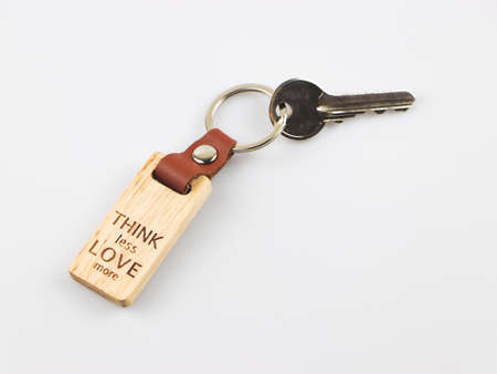 Close up image of wooden keyring with word Think less love more on white background.