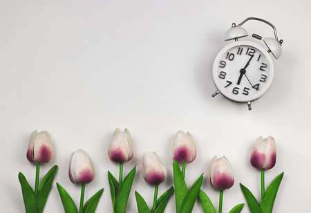 Top view or flat lay of white vintage alarm clock on white background with tulips decoration.の写真素材