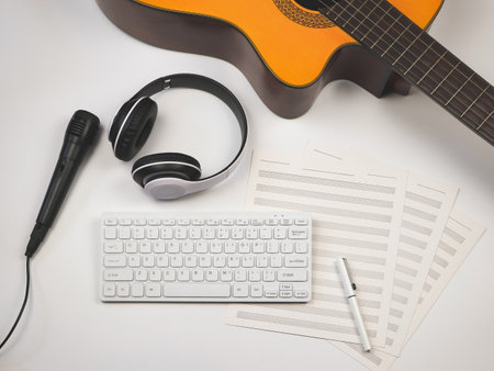 Top view or flat lay of computer keyboard, headphones, microphone, blank music sheets and acoustic guitar on white background. Online music lessons or musician concept.の写真素材