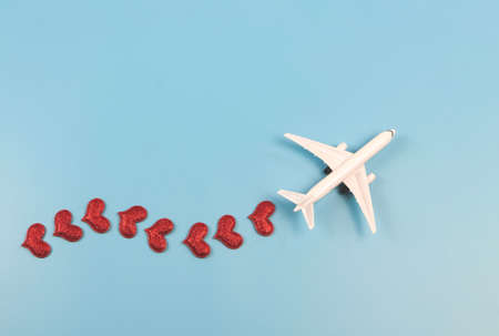 Top view or flat lay of airplane model with red hearts on blue background. Honeymoon trip or travel...
