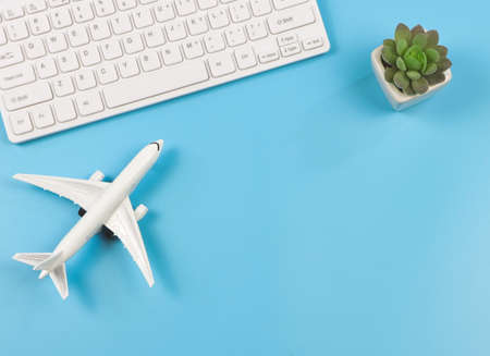 Top view or flat lay of airplane model, computer keyboard, and cactus on blue background, business...
