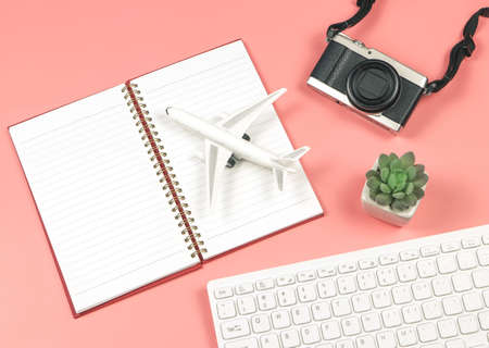 Top view or flat lay of airplane mode on opened notebook or diary, computer keyboard, camera and cactus on pink background, business and traveling concept.の写真素材