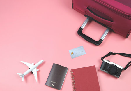 Top view or flat lay of airplane model, red diary , camera, passport, credit card  and pink suitcase on pink background. Travelling concept.の写真素材