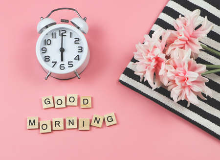 Top view or flat lay of white vintage alarm clock  with wooden letter "GOOD MORNING" and bouquet of pink flower on black and white stripes cloth on pink background.の写真素材