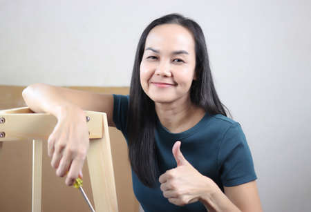 Portrait of Asian woman  trying to assemble knockdown furniture, showing her thumb up and smiling at camera.の写真素材