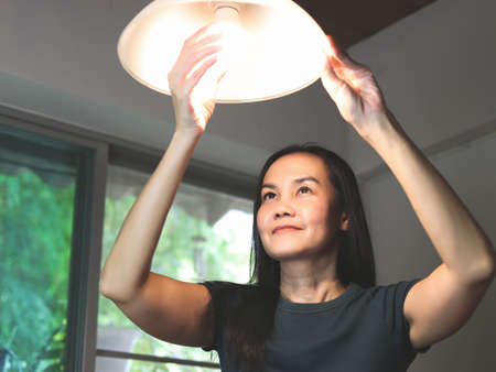 Cheerful Asian woman  changing light bulb in her house.の写真素材