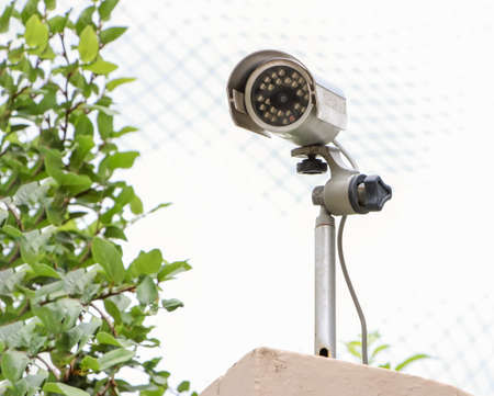 Old Security Camera, CCTV on location. Security camera on the wall  with sky and green plants background.の写真素材