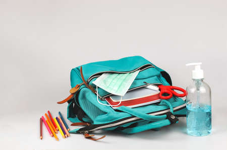 Front view  of  backpack with school supplies , medical mask and alcohol sanitizer gel on white  background with copy space. COVID-19 prevention while going back  to school  and new normal  concept.の写真素材