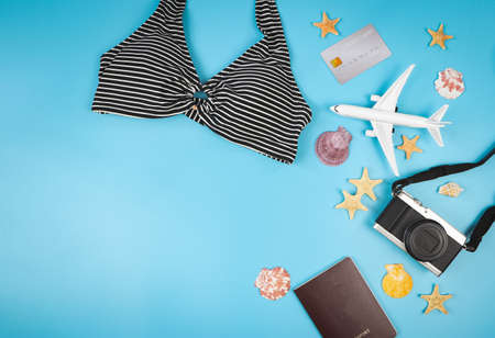 Top view or flat lay of   bikini, camera credit card, passport and airplane model on blue...