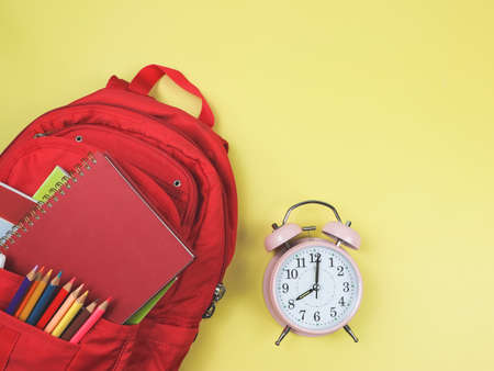 Top view or flat lay of red school backpack with school supplies  and pink vintage alarm clock 8 o'clock on yellow background with copy space. Back to school concept.の写真素材