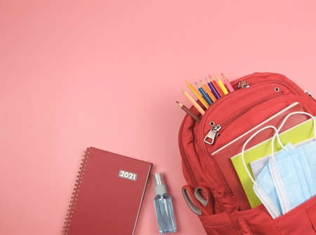 Top view or flat lay of red 2021 diary, red  backpack with school supplies , surgical mask and alcohol sanitizer spray on pink background.の写真素材