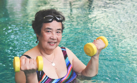Portrait of happy and healthy Asian senior woman with kickboard in a swimming pool. Smiling old...
