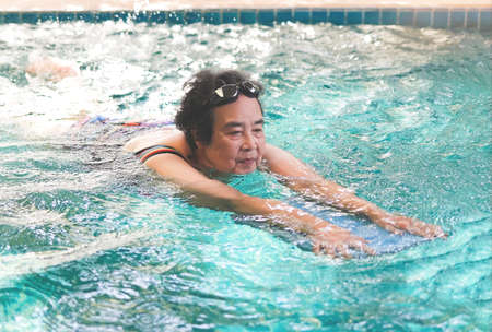 Portrait of happy and healthy Asian senior woman with kickboard in a swimming pool. Smiling old woman swimming with inflatable board in swimming pool.の写真素材