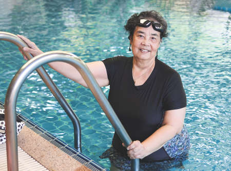Portrait of happy and healthy Asian senior woman wearing swimming wear and goggles, standing at...