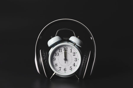 Front view of white vintage alarm clock show 12 o'clock cover with headphones on black background ,time to listen to music or scary story podcast background.の写真素材