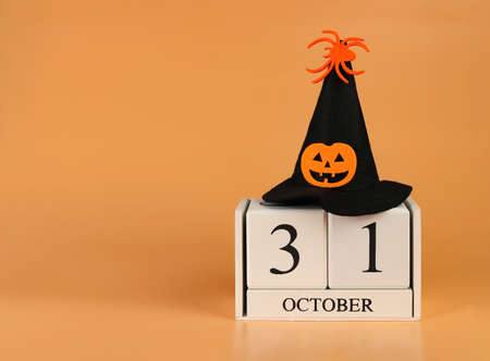 Front view of wooden calendar 31 October and Halloween witch hat decorated with pumpkin head and spider on orange background. Halloween costume concept.の写真素材