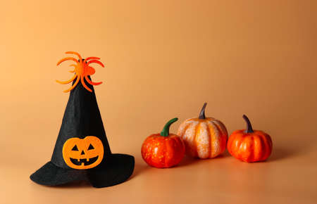 Front view of Halloween witch hat decorated with pumpkin head and spider with plastic pumpkins on orange background. Halloween costume party concept.の写真素材