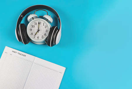 Top view or flat lay of habit tracker book,  vintage alarm clock cover with headphones  on blue background with copy space.の写真素材